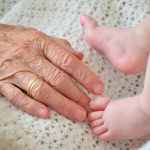 Hand einer alten Frau und Füße eines Babys als Symbol für Älterwerden