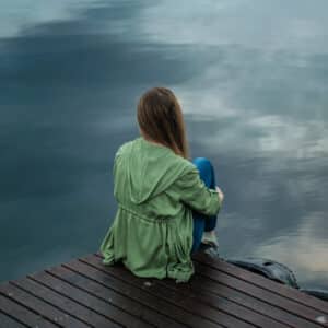 Frau, die alleine am Wasser sitzt, als Symbol für Einsamkeit