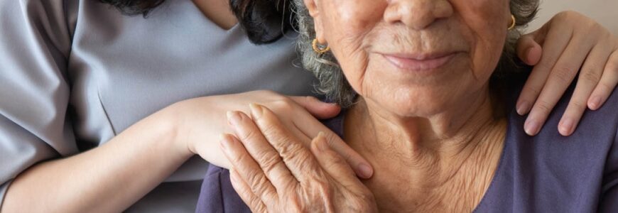 alte Frau hält lächelnd die Hand einer jungen Pflegerin