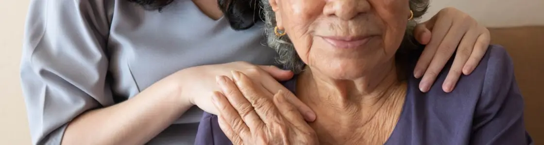 alte Frau hält lächelnd die Hand einer jungen Pflegerin