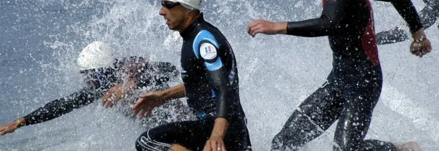 Gruppe Sportler im Neoprenanzug stürmt ins Wasser
