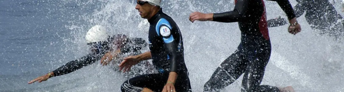 Gruppe Sportler im Neoprenanzug stürmt ins Wasser